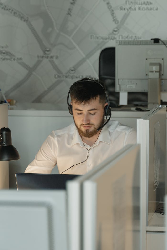 Caucasian man wearing black headphones working on a laptop in a call center office cubicle.